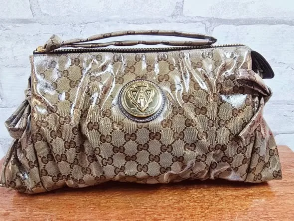 Metallic patterned Gucci clutch with a short brown handle on a wooden display